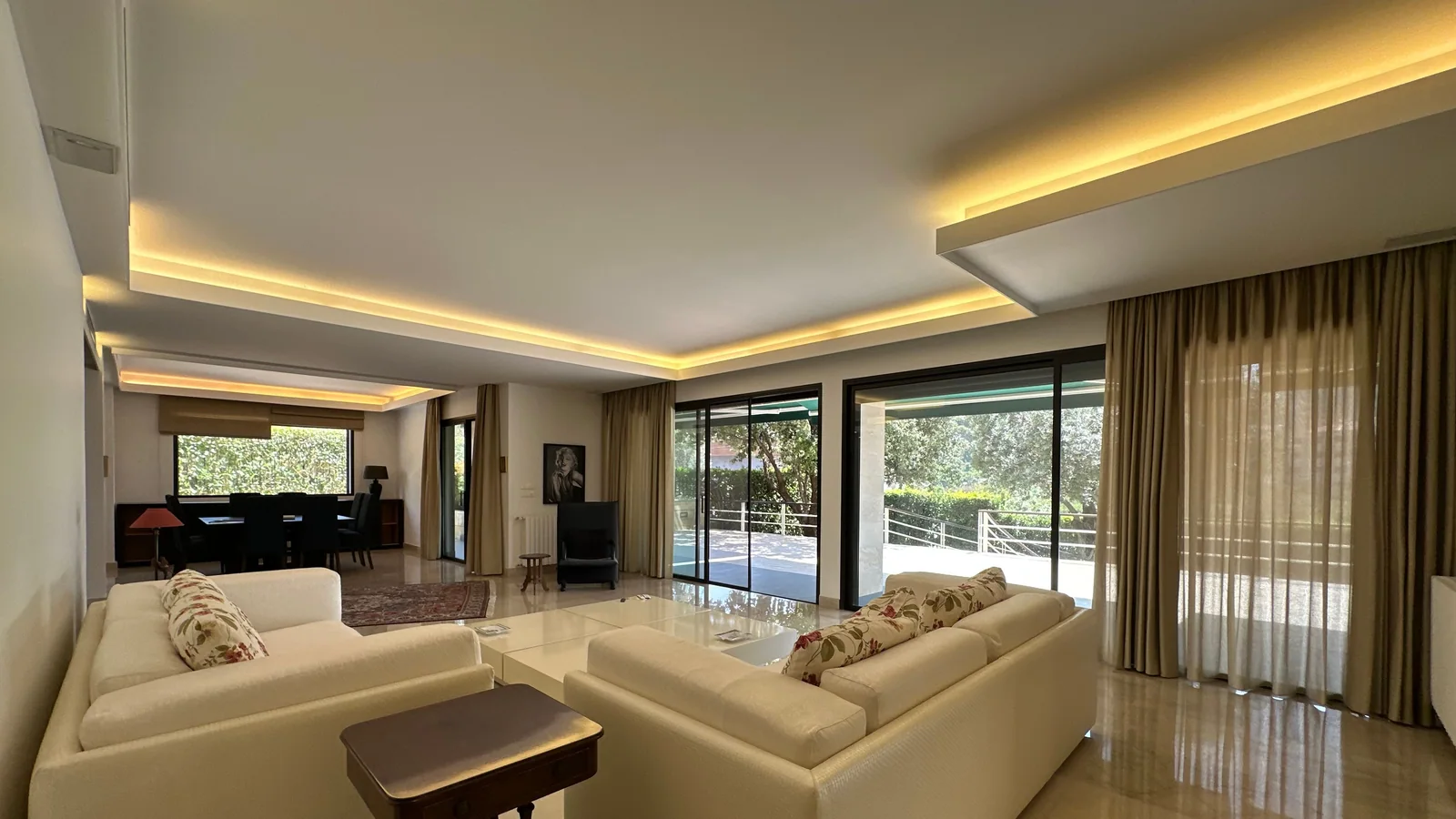 A luxury living room with layered cove lighting and full-height window treatments